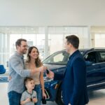 Family handing a key fob to a salesperson in a bright dealership showroom