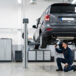 Technician inspecting the underbody of an SUV on a lift in a dealership workshop