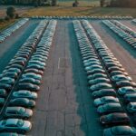 Aerial view of a dealership lot with rows of cars casting long shadows and one empty parking space